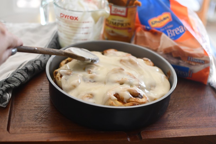 spreading cream cheese glaze on cinnamon rolls