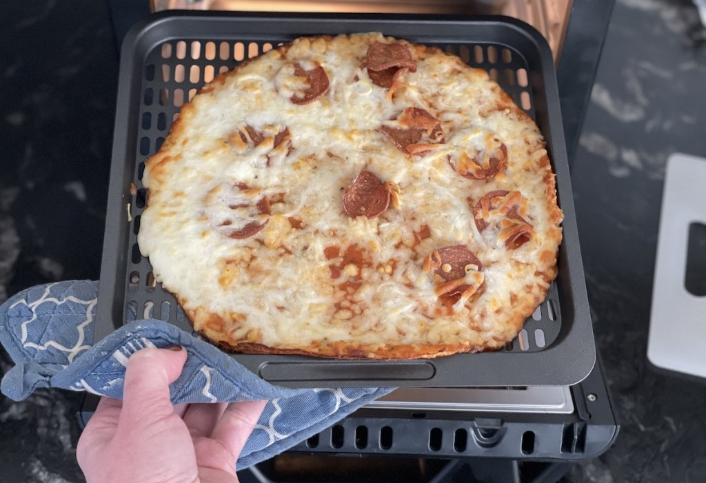 hand pulling out metal tray with cooked pizza from air fryer