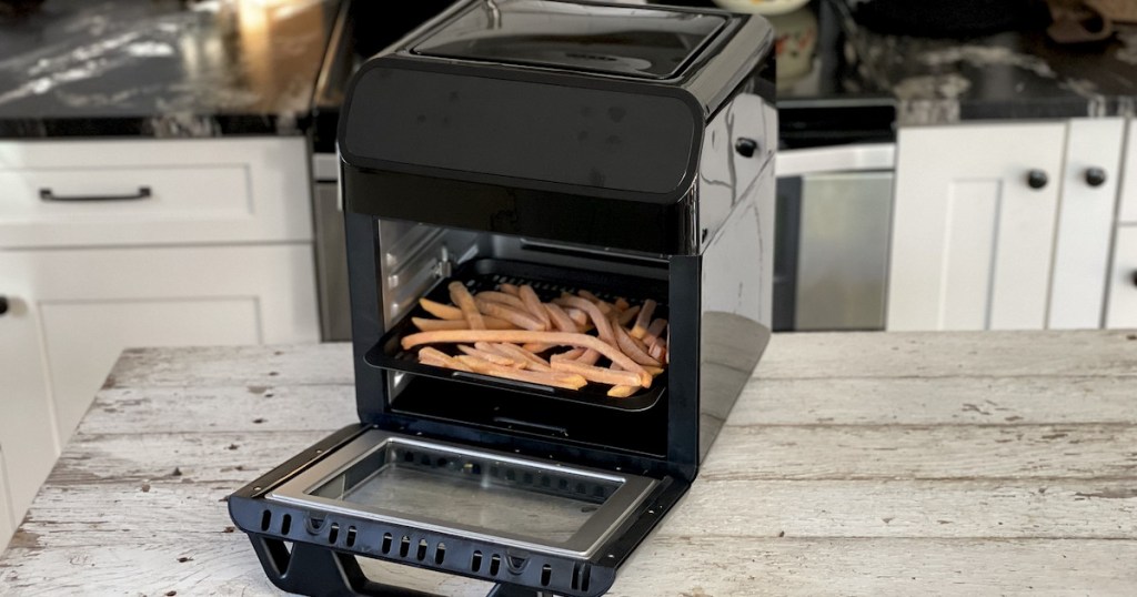 black air fryer with door open and frozen fries on tray on kitchen counter