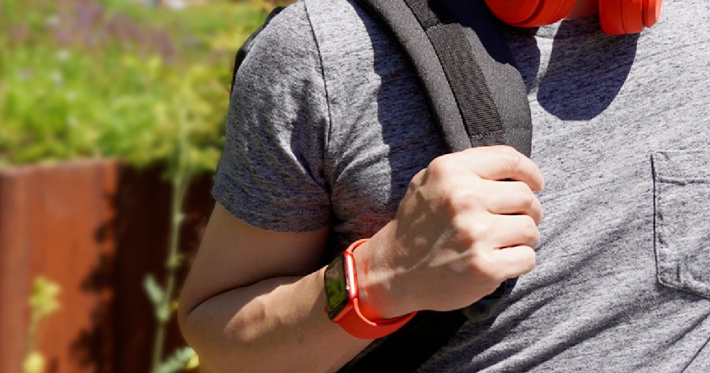 man wearing red smartwatch and holding backpack with red headphones around neck
