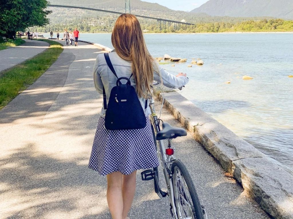 woman wearing Baggallini Metro backpack walking her bike