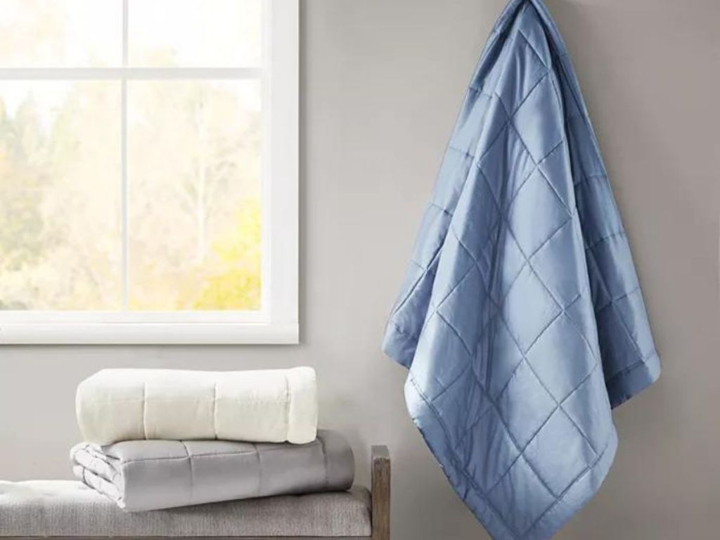 white and gray comforters folded and stacked and blue comforter hanging up