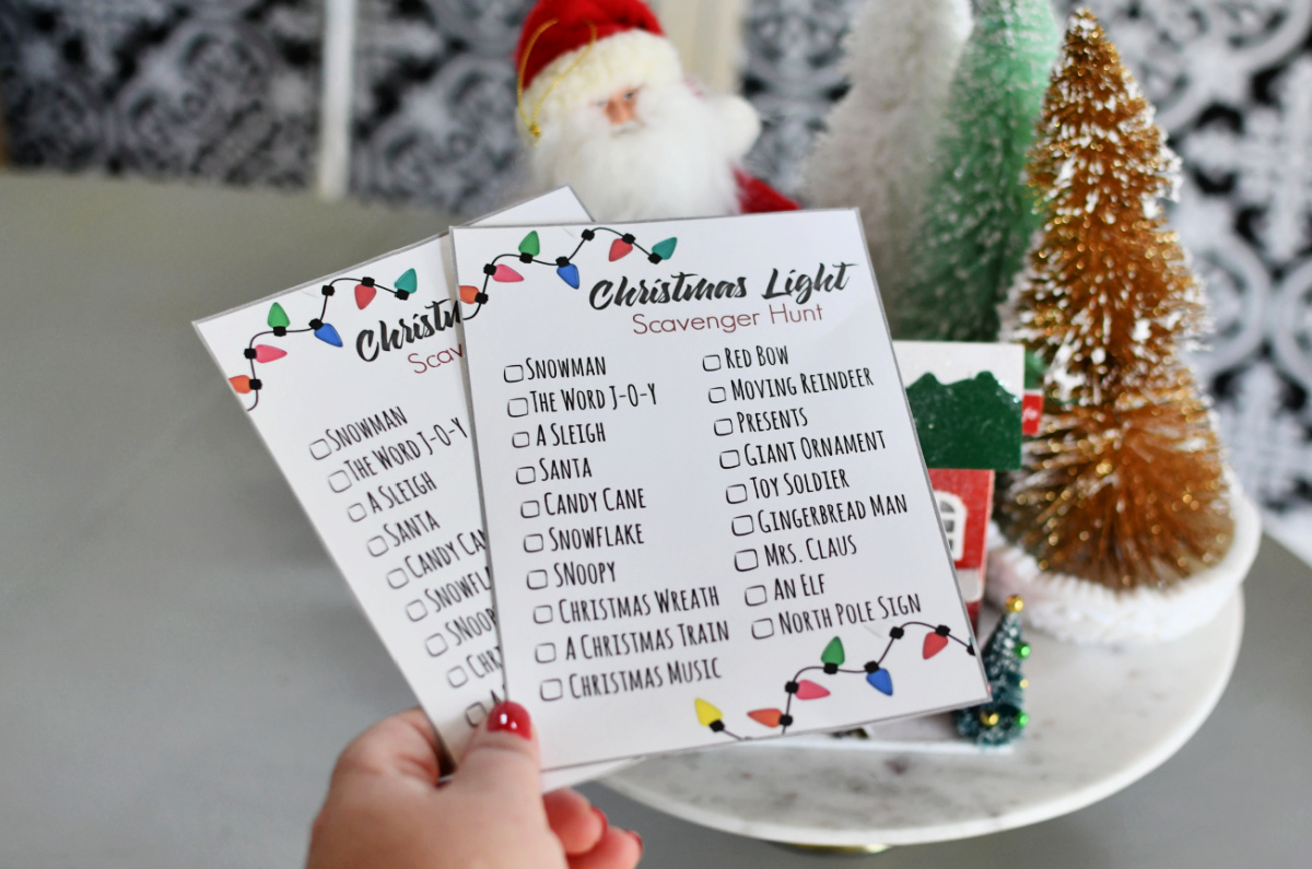 Hand holding up a Christmas Light Scavenger Hunt Free Printable in front of holiday decorations