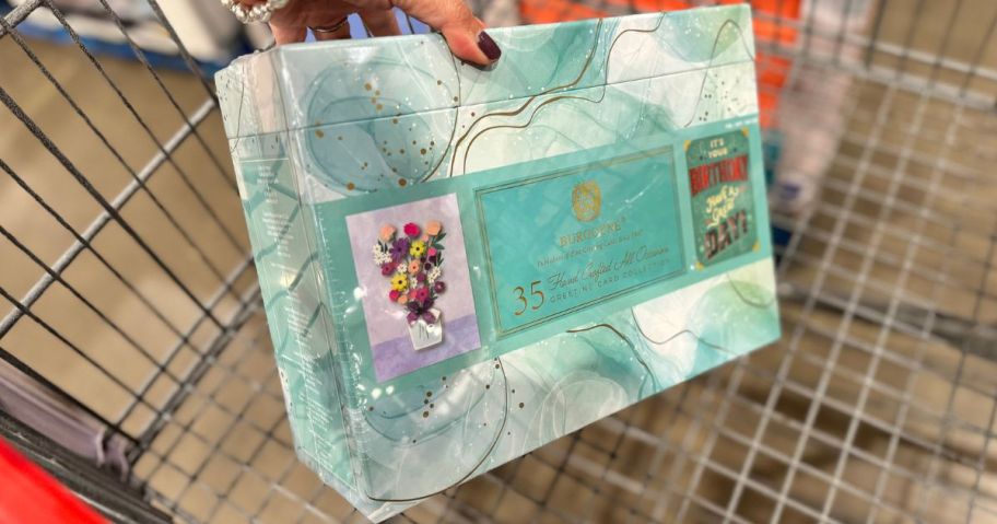 Hand putting a box of costco greeting cards into a shopping cart