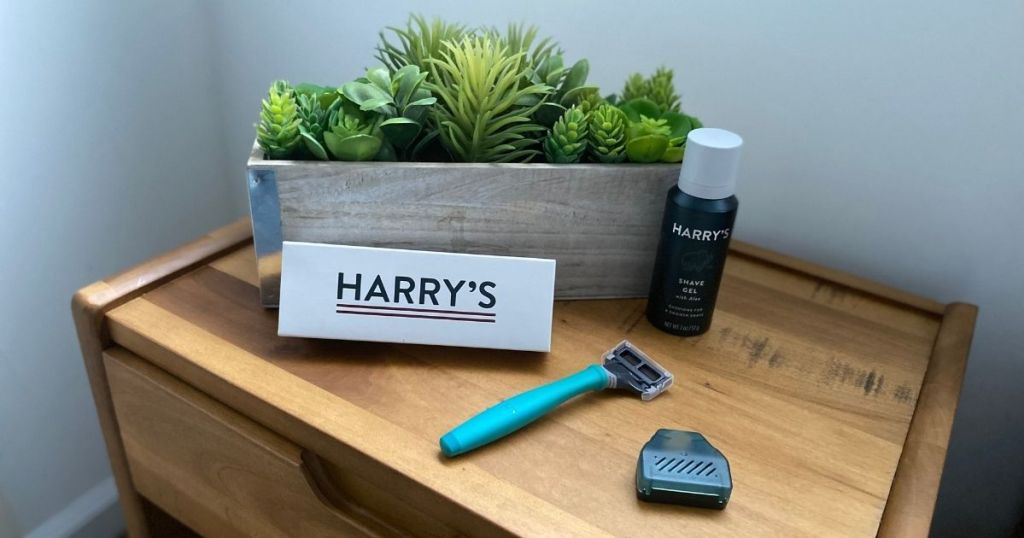 Harry's Shaving Kit with a razor, shavel gel, and travel case sitting on a table by a plant.