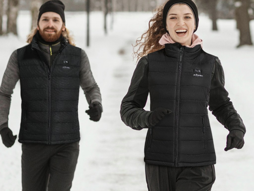 Man and woman running in snow, wearing black heated vest