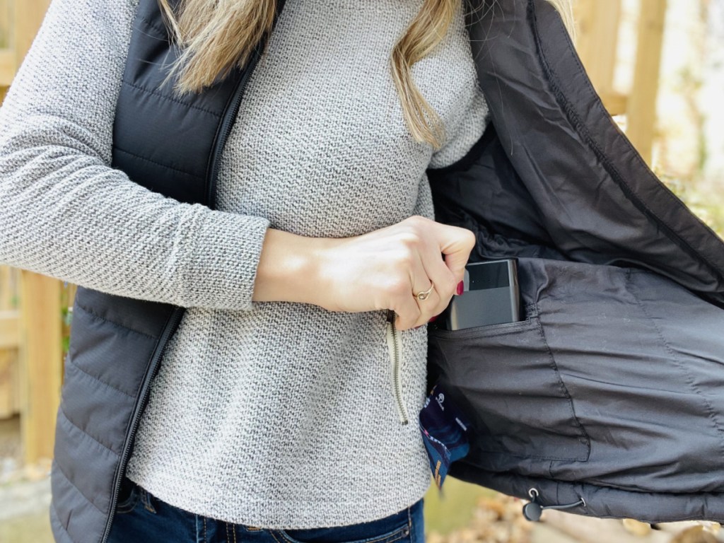 Woman placing a battery pack into internal pocket of black vest