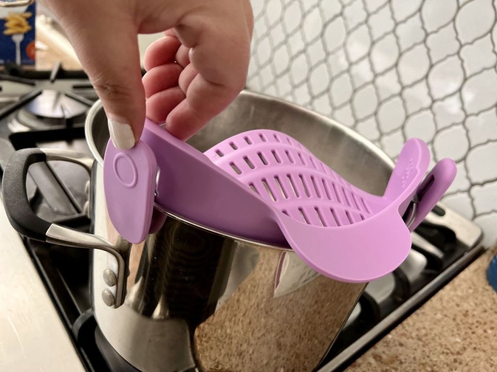  close up of purple Kitchen Gizmo Snap N Strain Adjustable Silicone Cup on pan