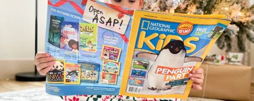 girl holding an open national geographic kids magazine in front of a christmas tree