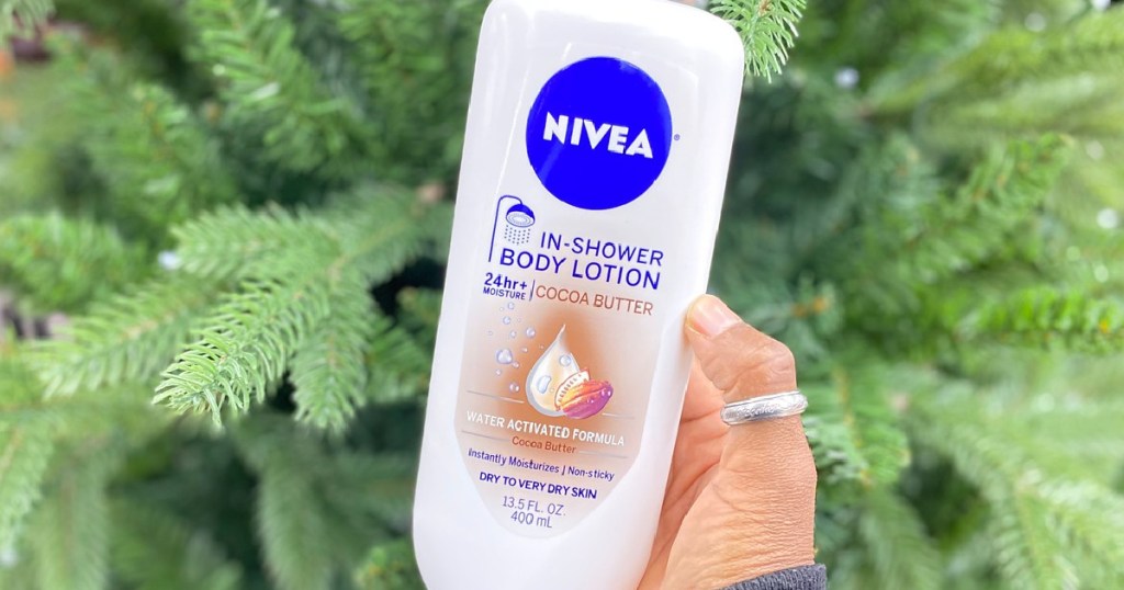 Hand holding a bottle of Nivea IN-Shower Body Lotion in front of indoor plant