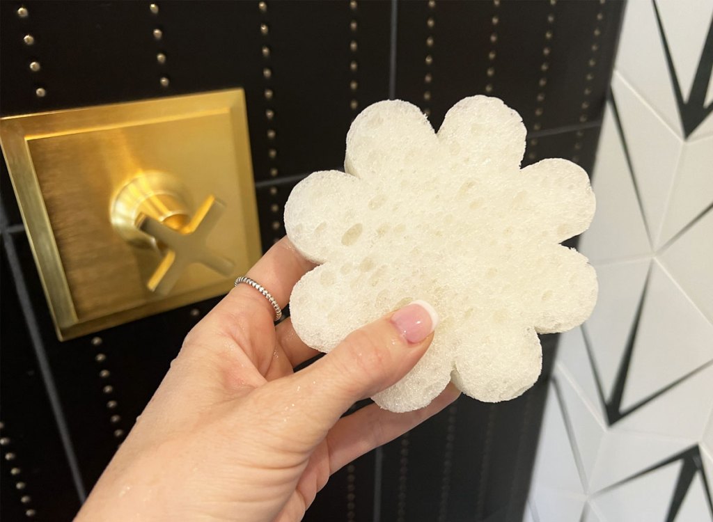 holding white flower shaped sponge in shower