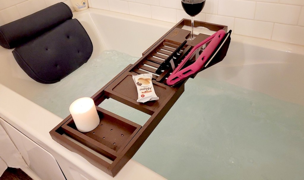 wood bathtub tray with ipad and glass of wine sitting over water filled bathtub