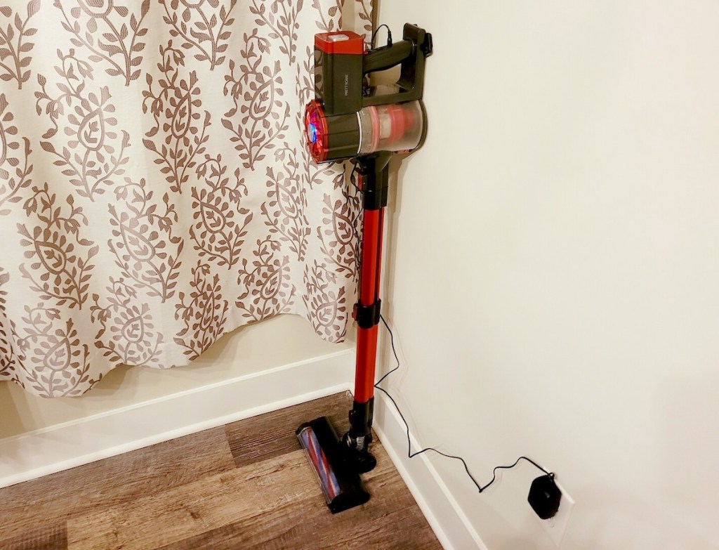 cordless red and black vacuum leaning on wall