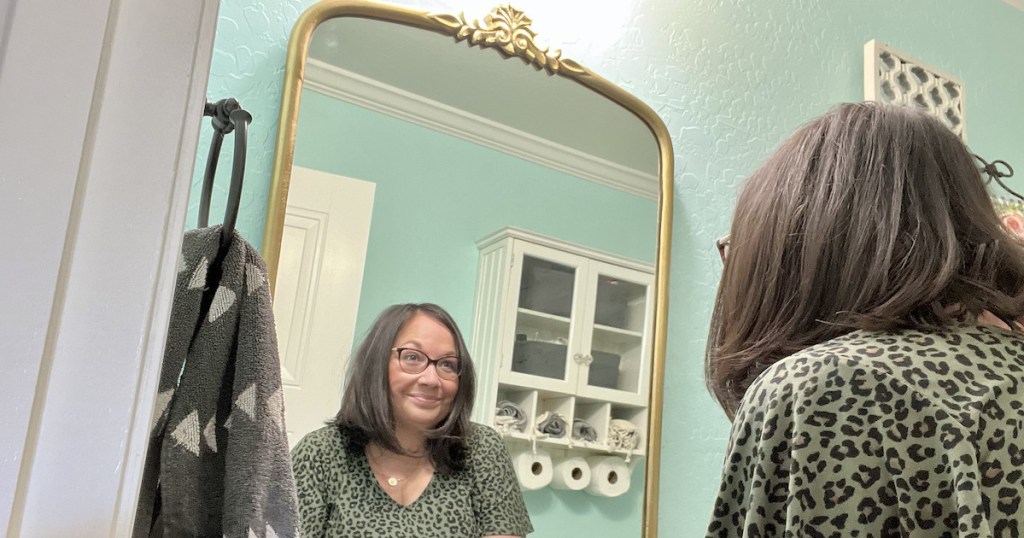 woman looking into gold anthropologie mirror lookalike hanging in bathroom