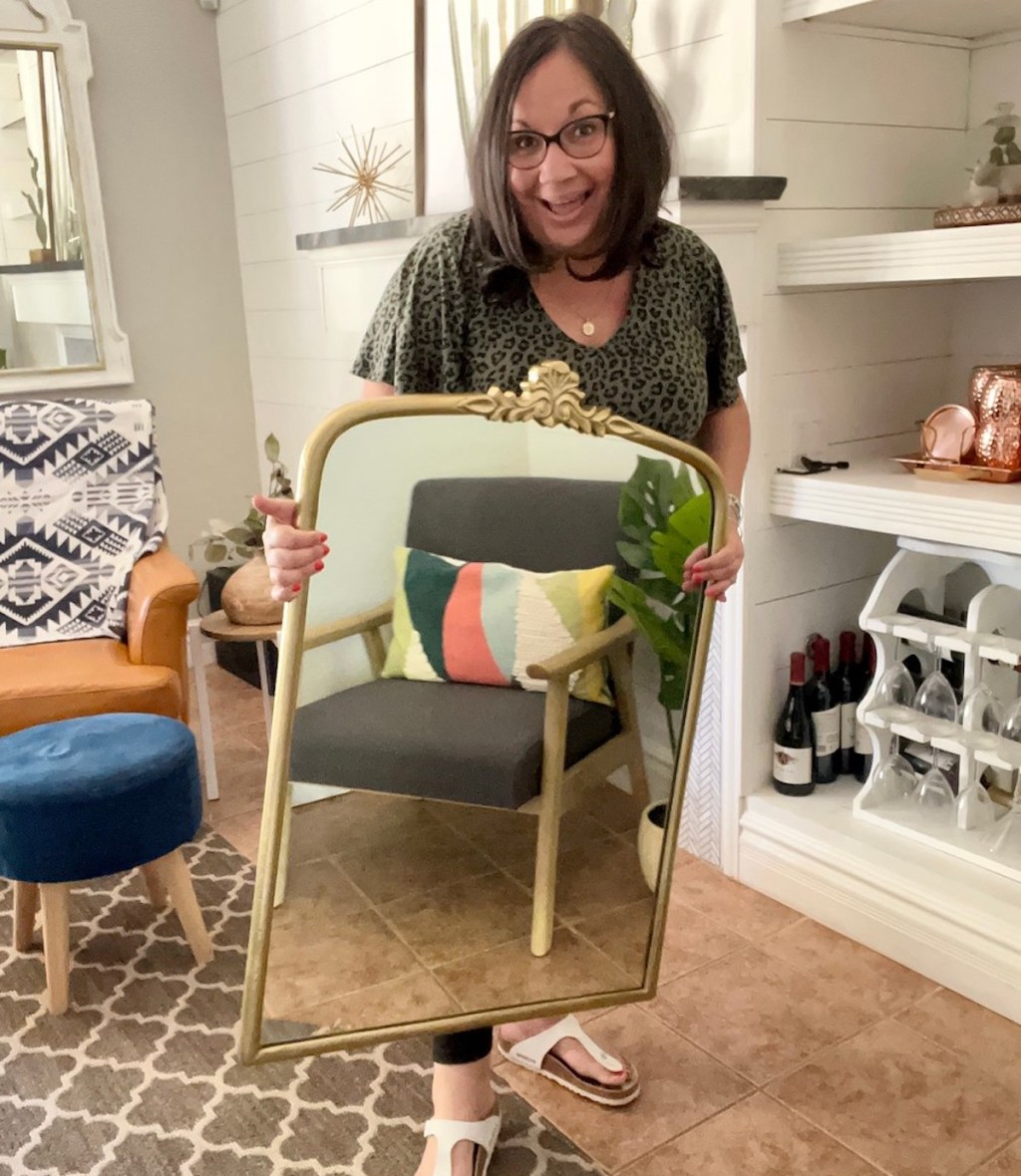 woman holding gold vintage Anthroplogie mirror lookalike in living room