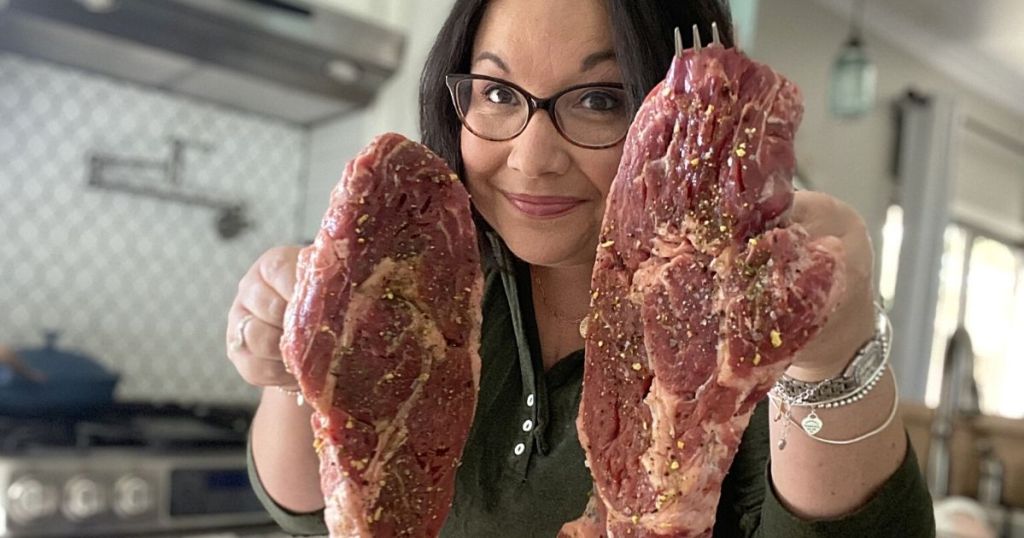 woman holding up 2 raw steaks