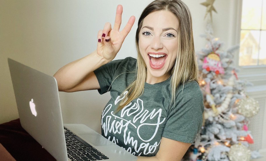 woman giving peace sign with hand while holding laptop