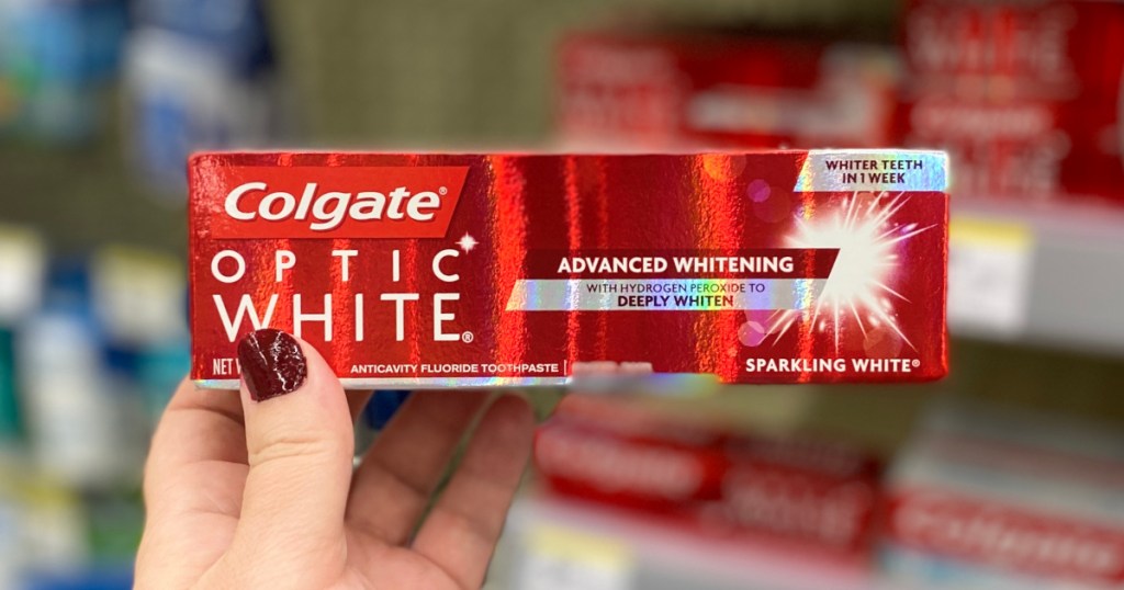 manicured hand holding box of Colgate brand toothpaste in store