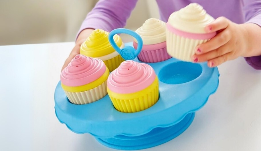 a little girls hand placing a cupcake in cupcake stand