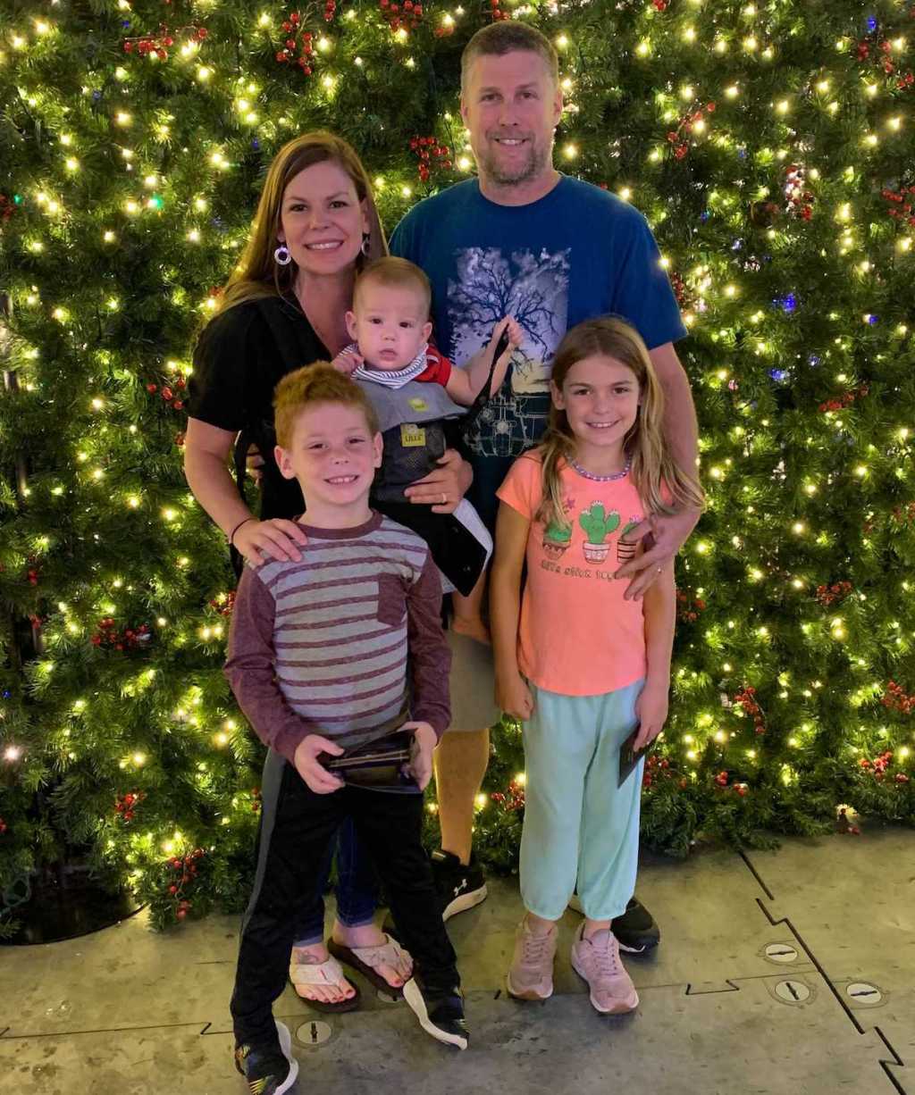 family of five standing in front of huge christmas tree