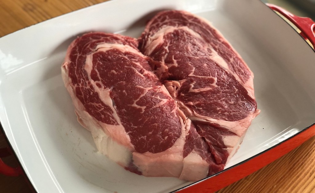 steak shaped like a heart sitting in white and red casserole dish