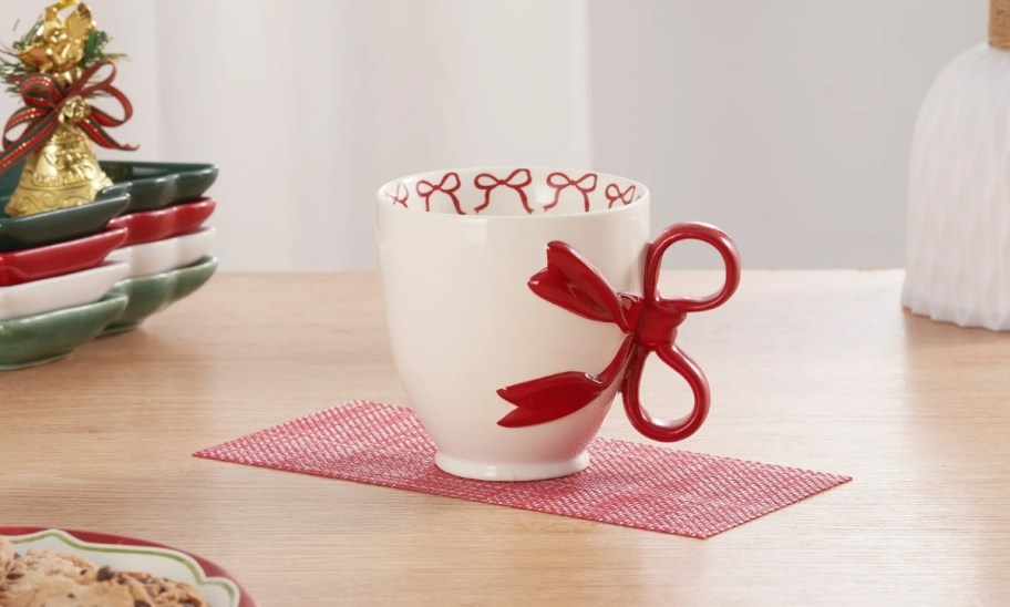 a white ceramic mug with a red bow handle 