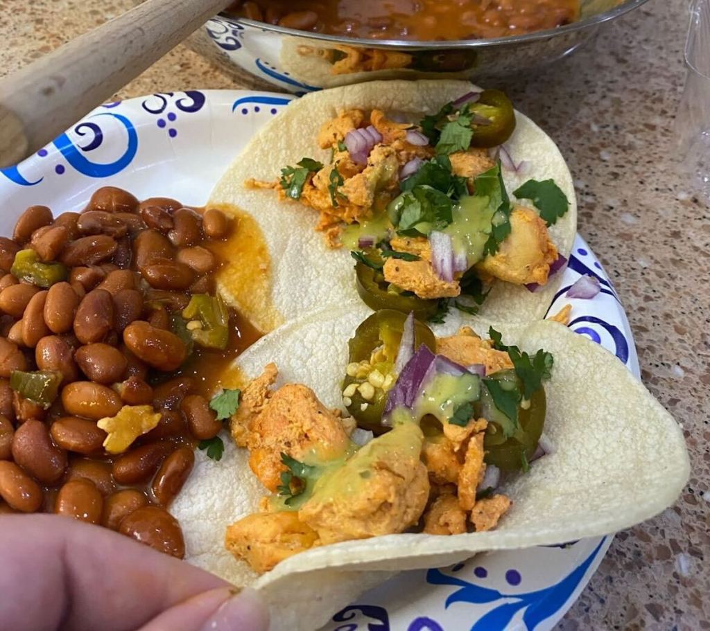 hand holding edge of tortilla shell with food and beans on plate