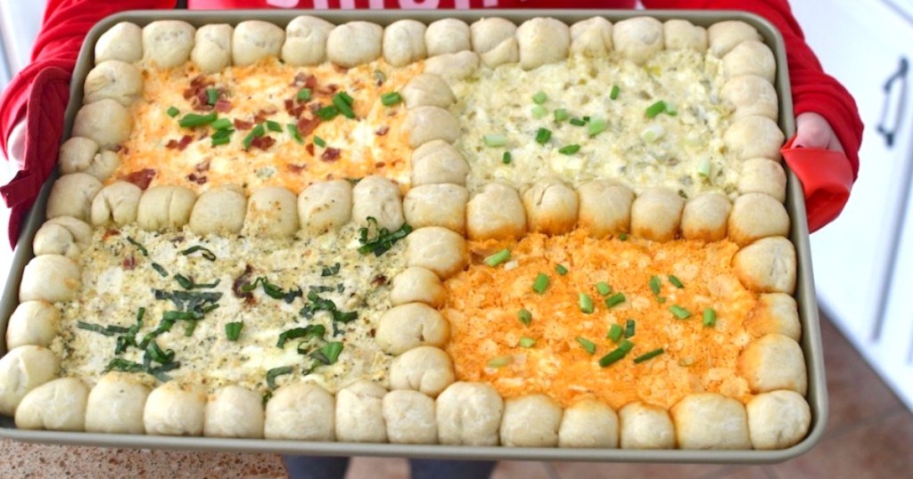 person holding sheet pan with four different dips and rolls of dough making border