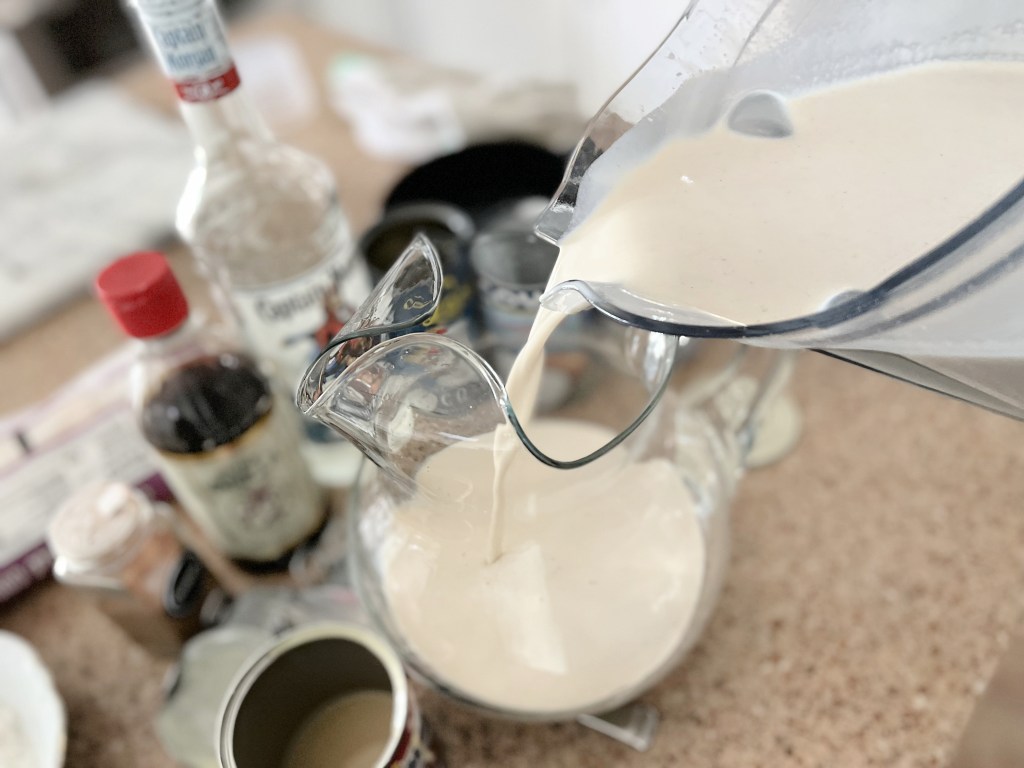 pouring coquito into a glass pitcher
