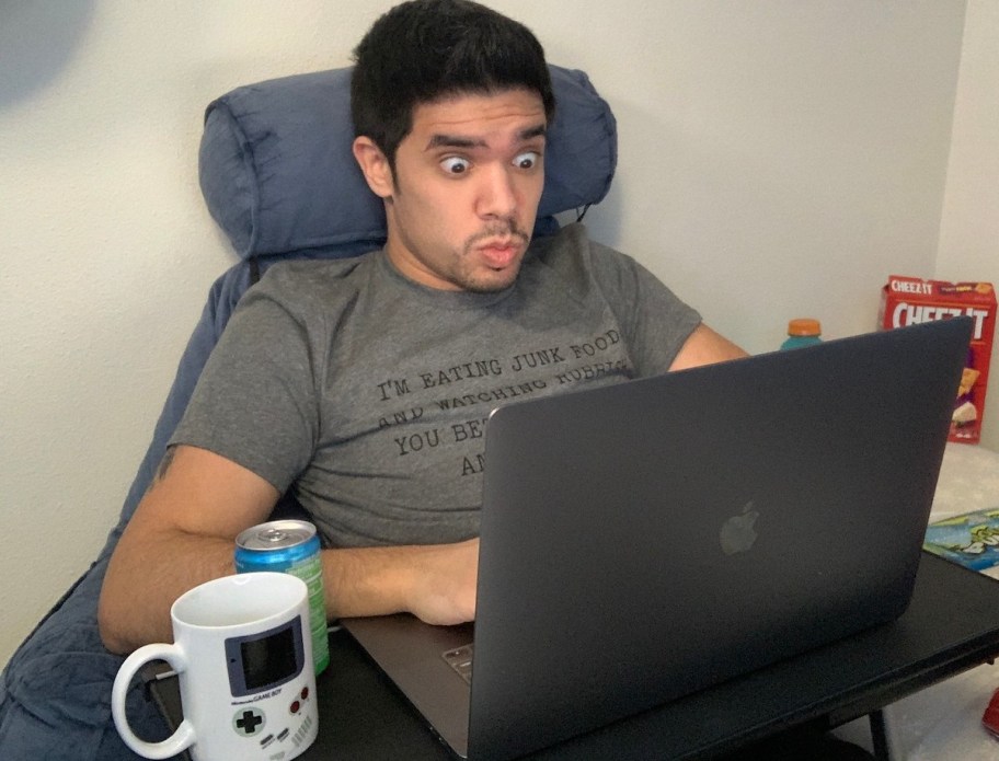 man sitting at laptop with surprised face and gaming coffee mug