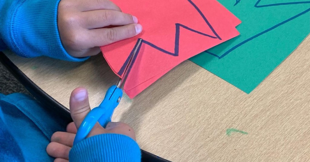 child using small blue scissors to cut construction paper