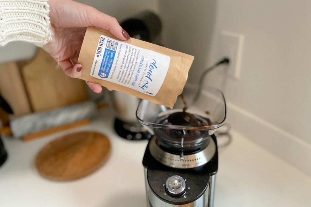 pouring whole bean coffee into a coffee grinder