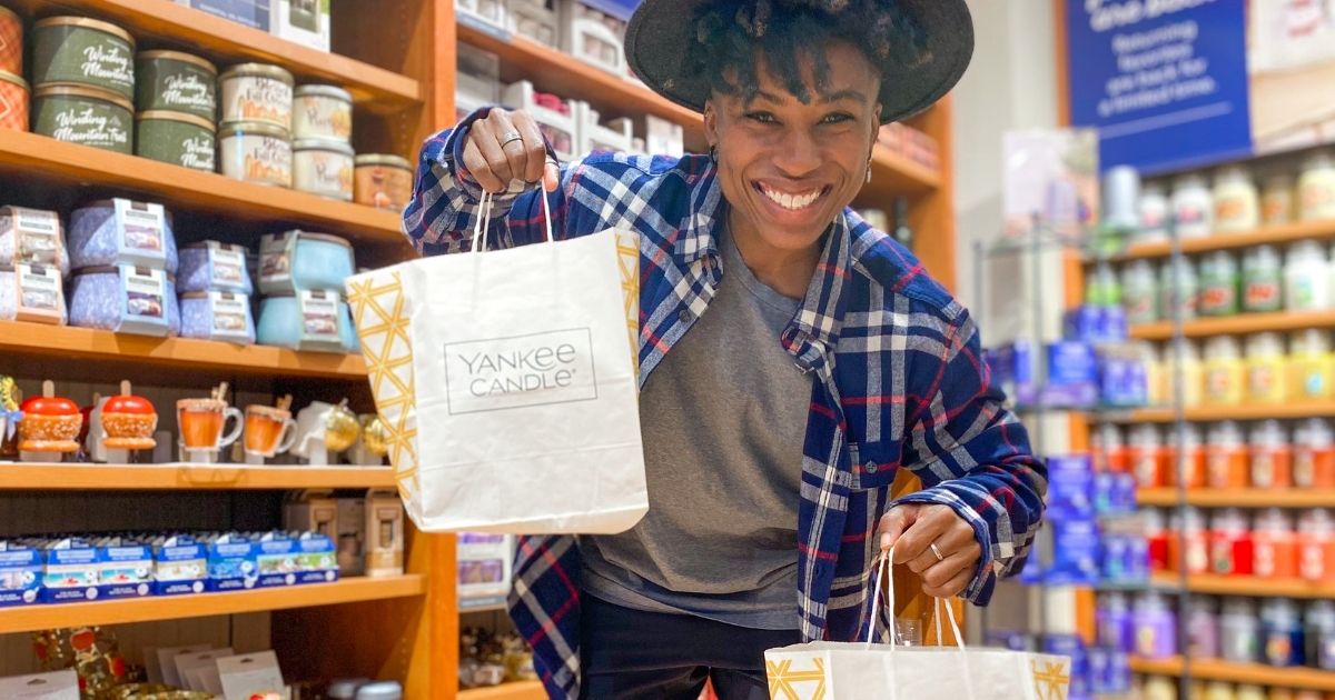 woman wearing a hat and flannel holding up yankee candle bags in a store