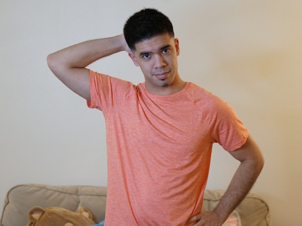 man waring orange shirt reaching up to his hair