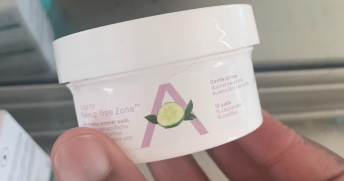 Hand holding a travel size container of Almay makeup remover pads