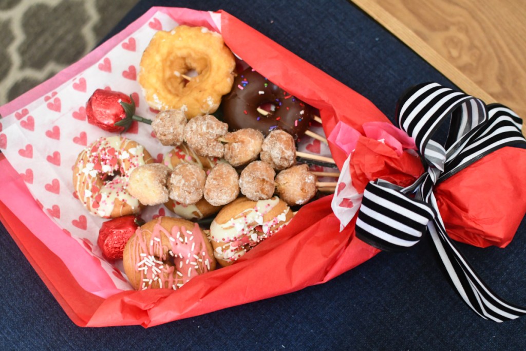 An edible arrangement of doughnuts with Valentine's Day tissue paper and a ribbon