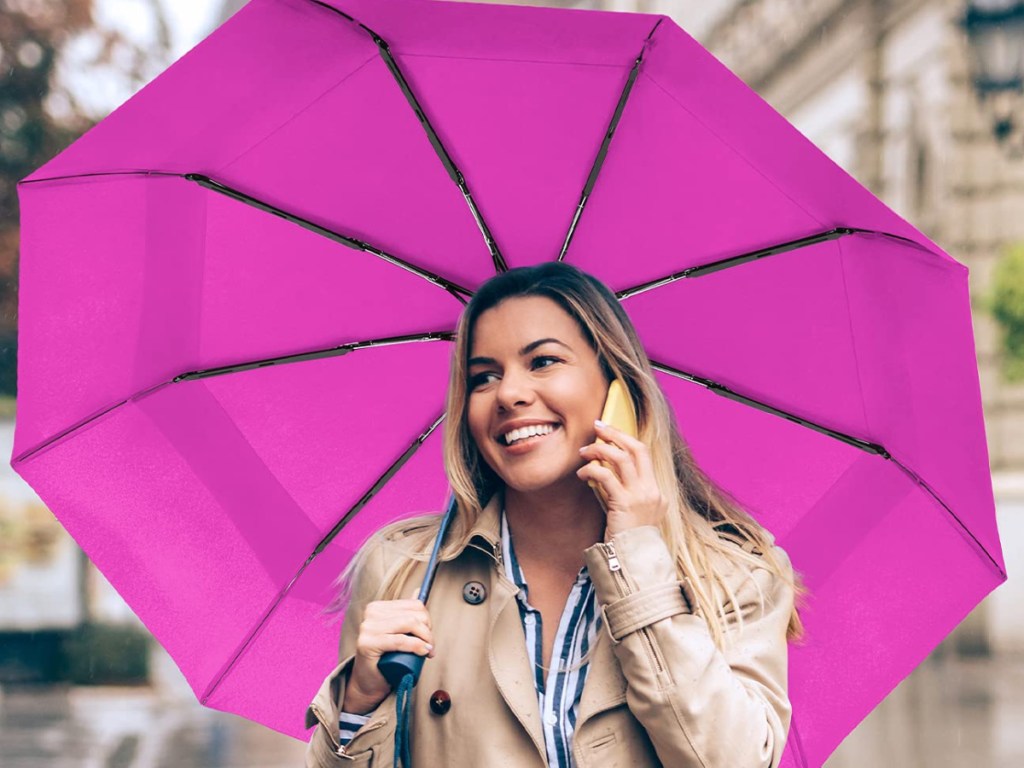 woman walking in rain on cell phone and using pink umbrella