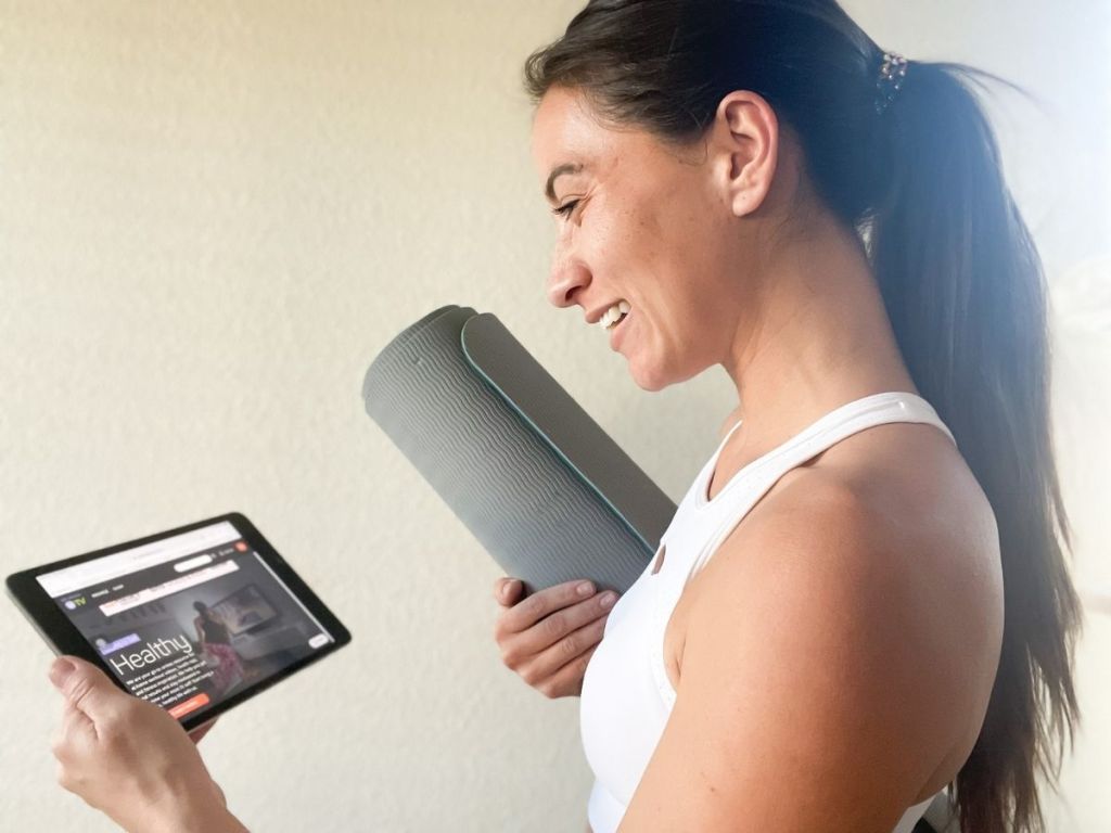 woman holding tablet in one hand and yoga mat in the other