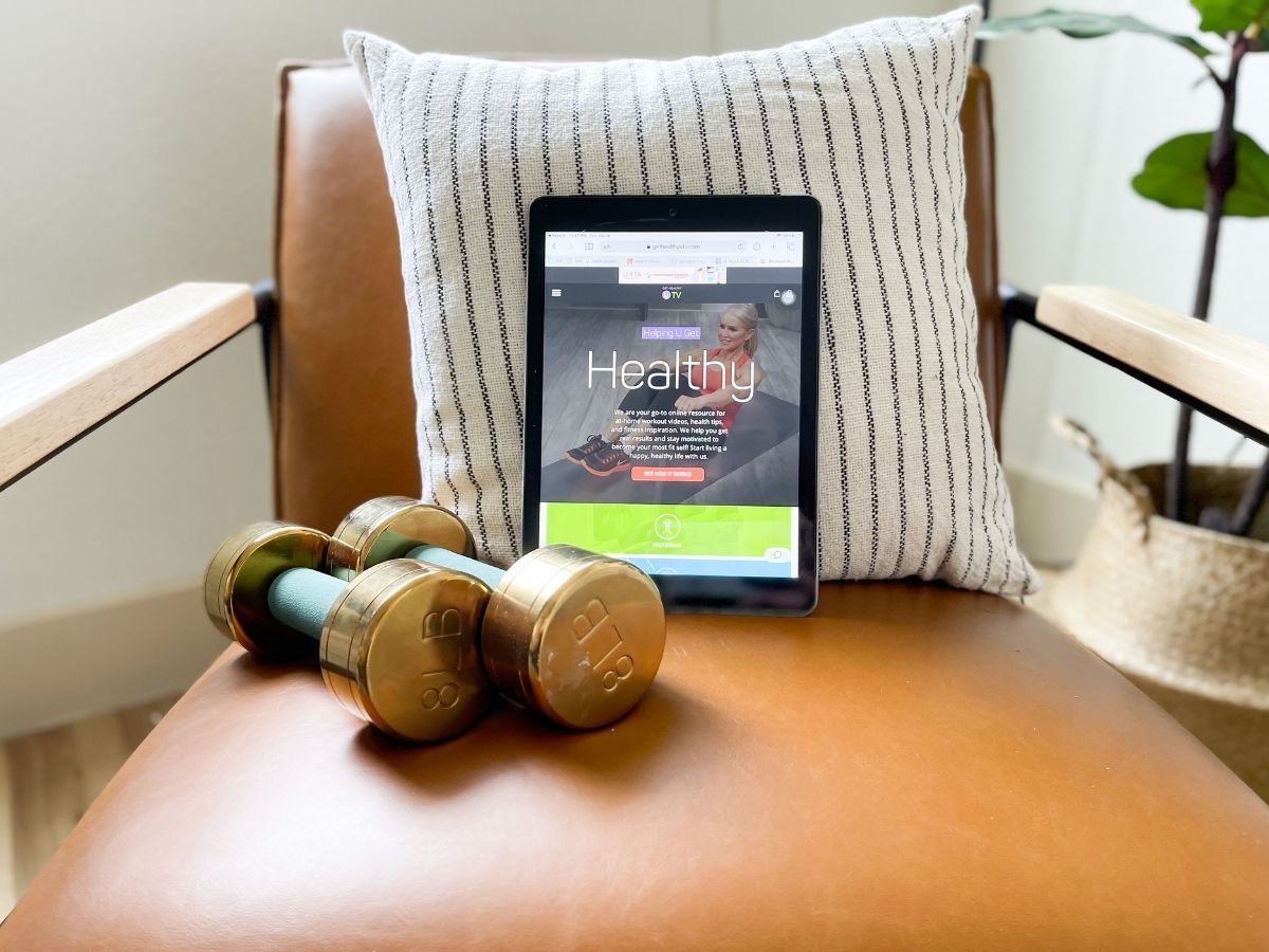 dumbbells, tablet and throw pillow on a tan accent chair