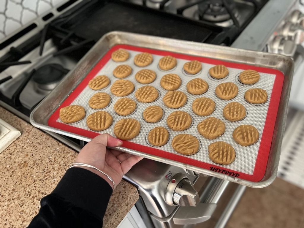 woman holding tray containing silicone baking mat and cookies