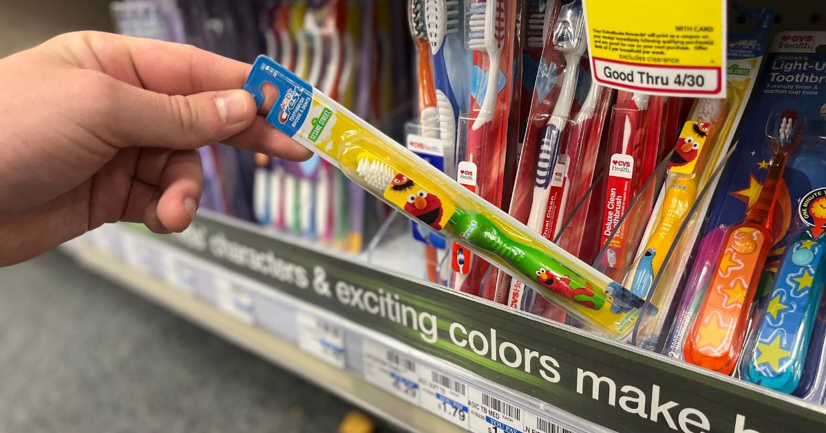 hand taking Crest Kid's Sesame Street Soft Bristles Toothbrush from store shelf