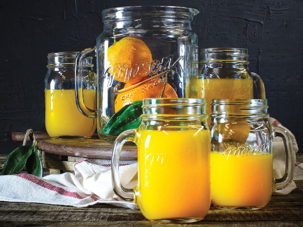 mason jar glass pitcher and four mason jar glasses filled with oranges and orange juice