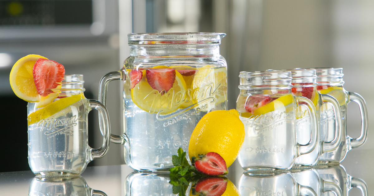 mason jar glass pitcher and four mason jar glasses filled with water, lemon and strawberries