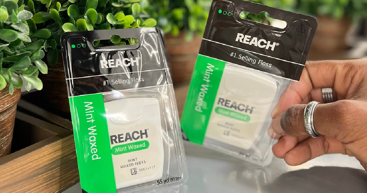 hand lifting a package of Reach Floss off a table from next to another package of floss