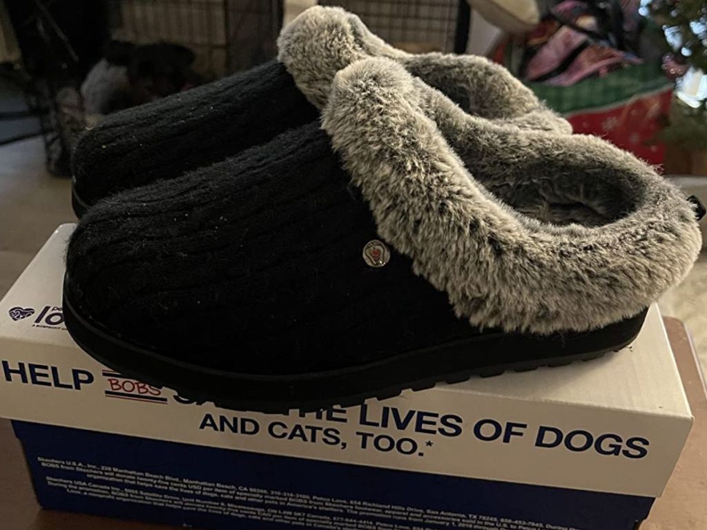 pair of black Skechers slippers with grey faux fur lining sitting on a shoe box