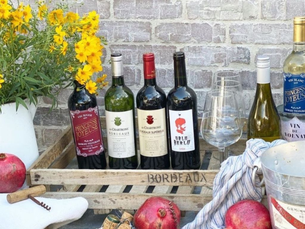 6 wine bottles in wooden crate in front of brick wall