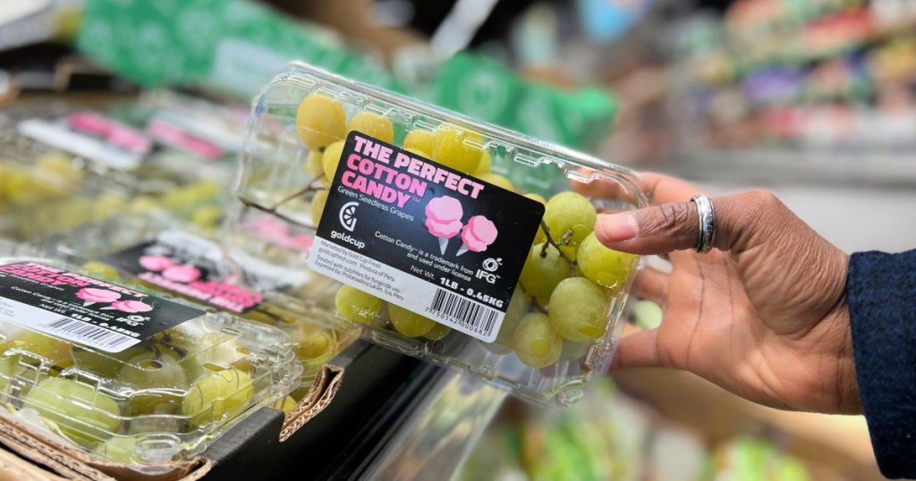 hand holding a box of cotton candy grapes near a store display