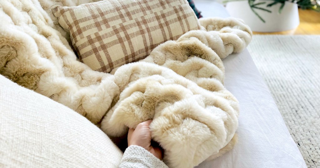 hand holding corner of faux fur throw blanket on white couch