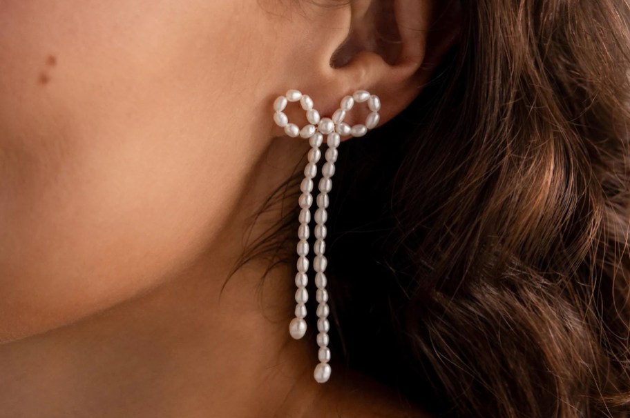 close up of white pearl bow earrings on womans ear