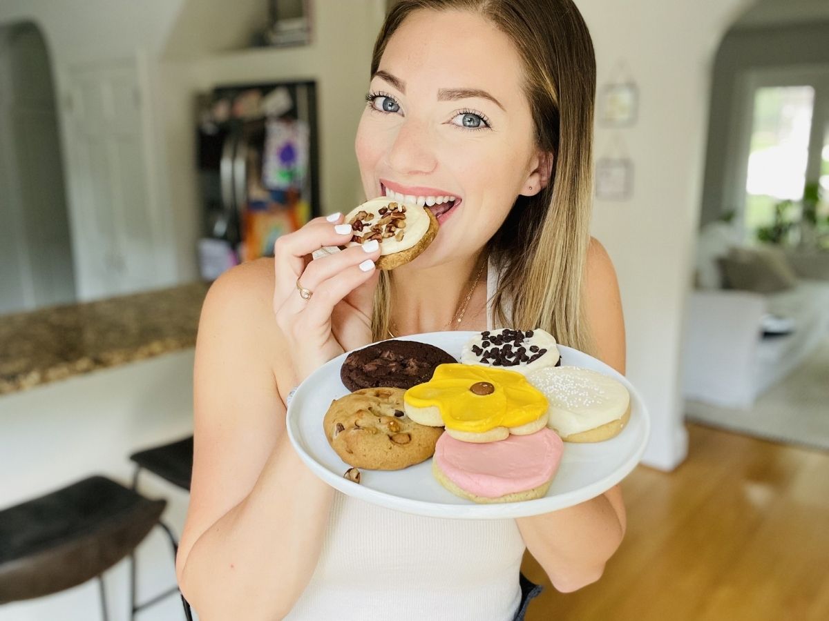 woman holding plate of cookies and eating cookie